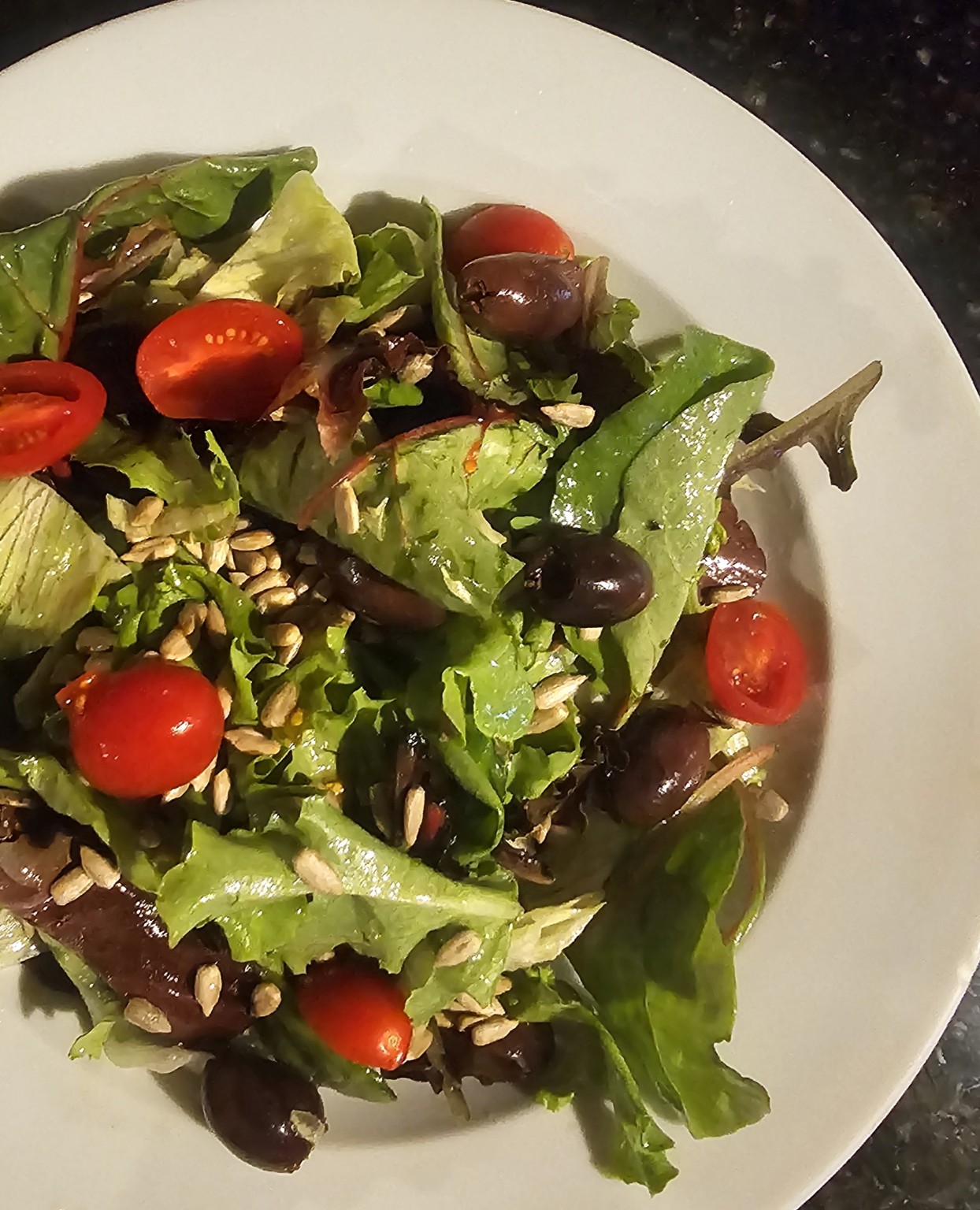 J5 salad with mixed greens, cherry tomatoes and olives on a white plate